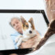 A female vet speaking to a client holding a dog through a tablet.